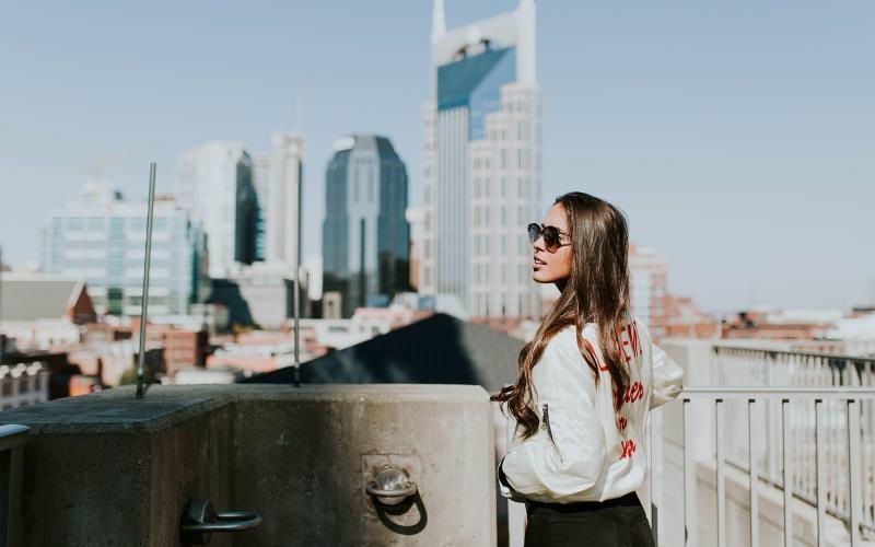 woman with sunglasses stands on a rooftop overlooking the city