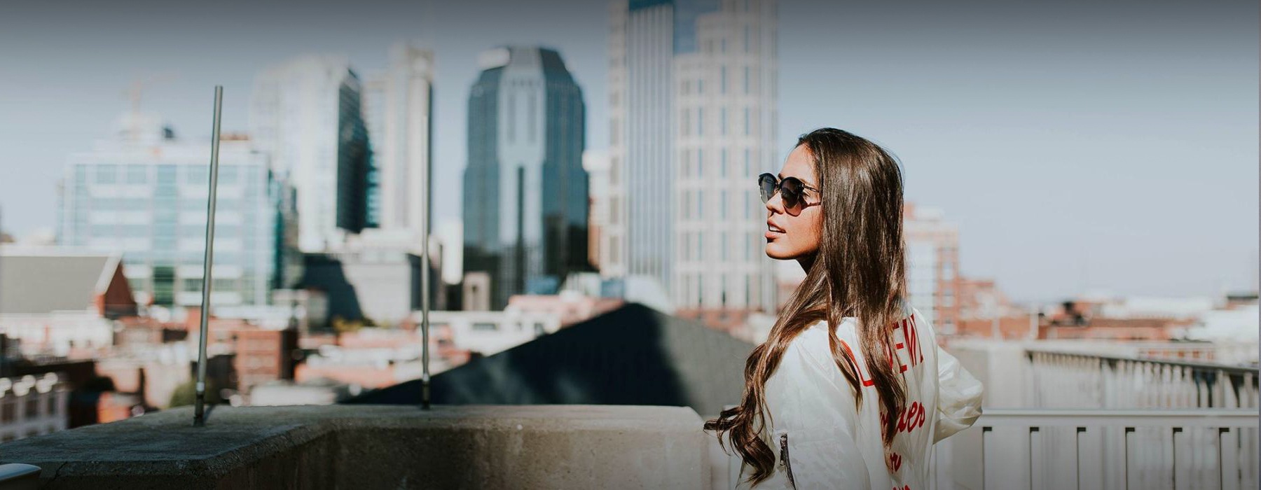 woman with sunglasses stands on a rooftop overlooking the city